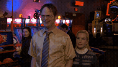 A Man And A Woman Are Standing In An Arcade With A Sign That Says ' Basketball ' On It GIF