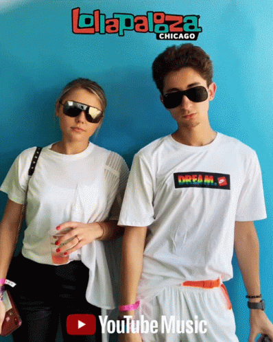 A Man And A Woman Are Standing In Front Of A Blue Wall That Says Lollapaloza Chicago On It GIF