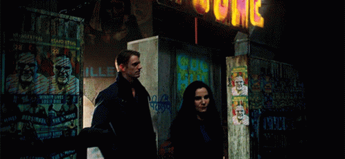 A Man And A Woman Are Standing In Front Of A Building With A Sign That Says ' Jc ' GIF