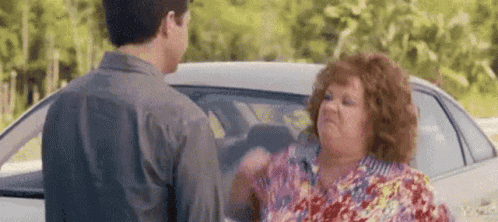 A Man And A Woman Are Standing In Front Of A Car . GIF
