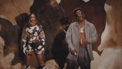 A Man And A Woman Are Standing In Front Of A Cow Skin GIF