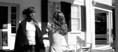 A Man And A Woman Are Standing In Front Of A House . GIF