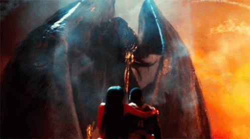 A Man And A Woman Are Standing In Front Of A Large Monster GIF