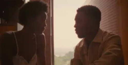 A Man And A Woman Are Standing In Front Of A Mirror Looking At Each Other . GIF