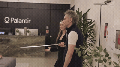 A Man And A Woman Are Standing In Front Of A Palantir Sign GIF