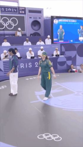 A Man And A Woman Are Standing In Front Of A Sign That Says ' Paris 2024 ' On It GIF