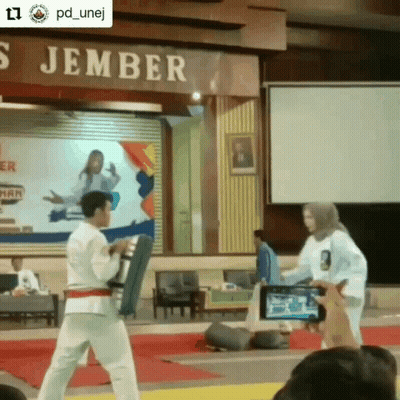 A Man And A Woman Are Standing In Front Of A Sign That Says ' S Jember ' On It GIF
