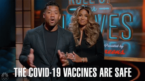 A Man And A Woman Are Standing In Front Of A Sign That Says " The Covid-19 Vaccines Are Safe " GIF