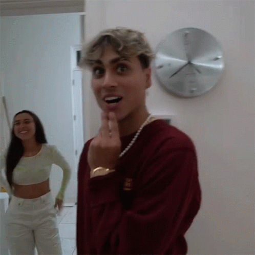 A Man And A Woman Are Standing In Front Of A Wall Clock . GIF