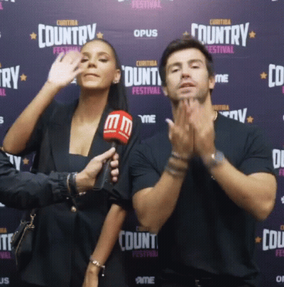 A Man And A Woman Are Standing In Front Of A Wall That Says Country Festival GIF