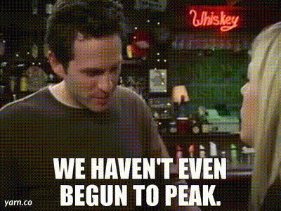 A Man And A Woman Are Standing In Front Of A Whiskey Sign And Talking To Each Other . GIF