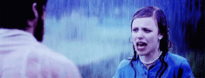 A Man And A Woman Are Standing In The Rain . The Woman Is Wearing A Pearl Necklace And A Blue Shirt . GIF