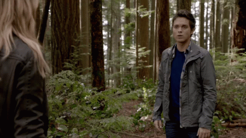 a man and a woman are standing in the woods and the man is wearing a grey jacket