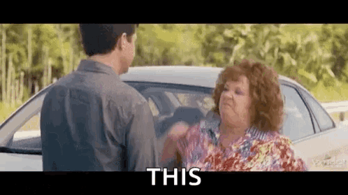 A Man And A Woman Are Standing Next To A Car And The Woman Is Holding The Man 'S Hand . GIF