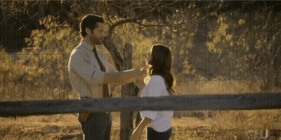 A Man And A Woman Are Standing Next To A Fence GIF