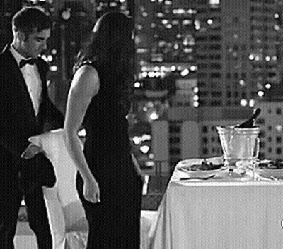 A Man And A Woman Are Standing Next To A Table With A Bottle Of Champagne . GIF