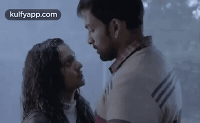 A Man And A Woman Are Standing Next To Each Other And Kissing In The Rain . GIF