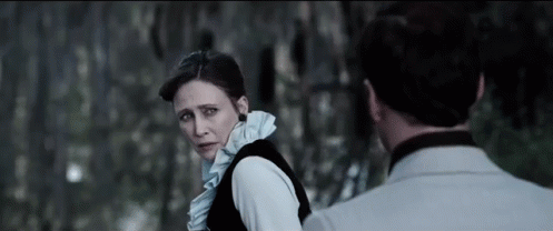 A Man And A Woman Are Standing Next To Each Other And Looking At Each Other In A Dark Room . GIF