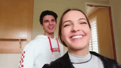 A Man And A Woman Are Standing Next To Each Other And Smiling . The Woman Is Wearing A Vans Sweatshirt . GIF