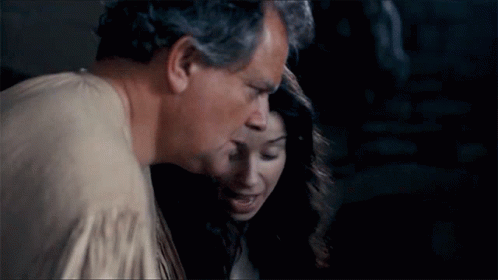 A Man And A Woman Are Standing Next To Each Other And The Man Is Kissing The Woman On The Cheek . GIF