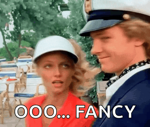 A Man And A Woman Are Standing Next To Each Other And The Man Is Wearing A Captain 'S Hat .. GIF
