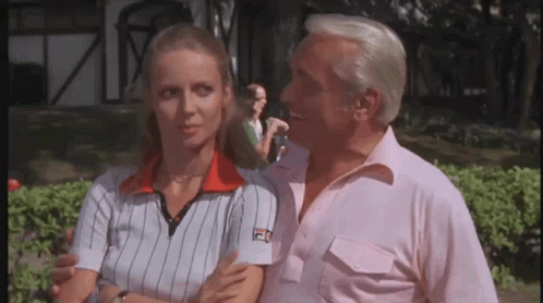A Man And A Woman Are Standing Next To Each Other And The Man Is Wearing A Fila Shirt . GIF