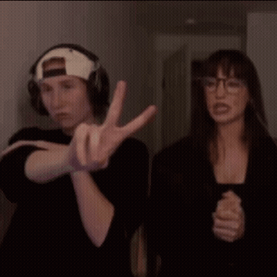 A Man And A Woman Are Standing Next To Each Other And The Man Is Wearing Headphones And The Woman Is Wearing Glasses GIF