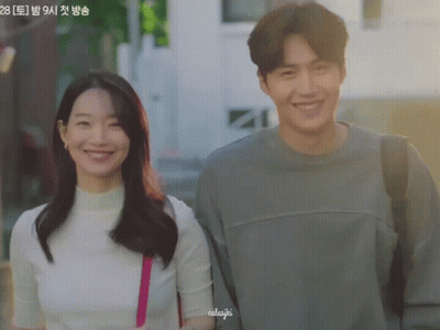 A Man And A Woman Are Standing Next To Each Other And The Woman Has A Pink Purse On Her Shoulder And The Man Is Smiling GIF