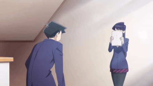 A Man And A Woman Are Standing Next To Each Other And The Woman Is Holding A Piece Of Paper In Front Of Her Face GIF