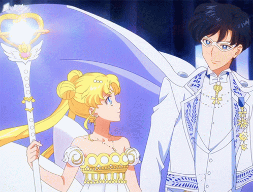 A Man And A Woman Are Standing Next To Each Other And The Woman Is Holding A Wand With A Heart On It GIF