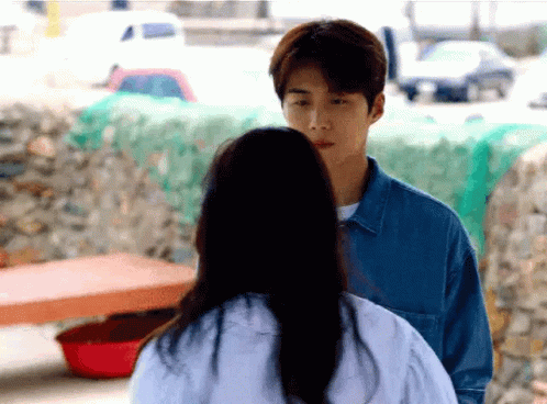 A Man And A Woman Are Standing Next To Each Other And The Woman Is Looking At The Man . GIF