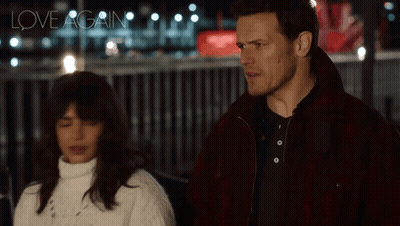 A Man And A Woman Are Standing Next To Each Other And The Words Love Again Are Visible In The Background GIF