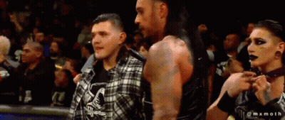 A Man And A Woman Are Standing Next To Each Other In A Crowd GIF