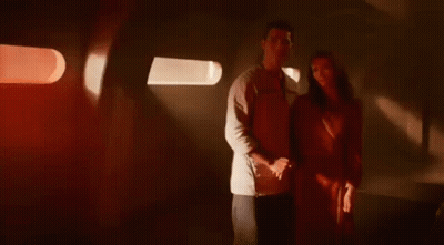 A Man And A Woman Are Standing Next To Each Other In A Dark Room Holding Hands . GIF