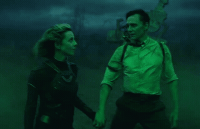 A Man And A Woman Are Standing Next To Each Other In A Dark Room Holding Hands . GIF