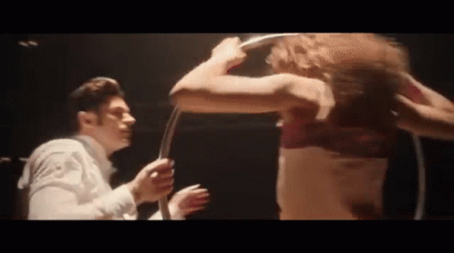 A Man And A Woman Are Standing Next To Each Other In A Dark Room . The Woman Is Wearing A Red Bra . GIF