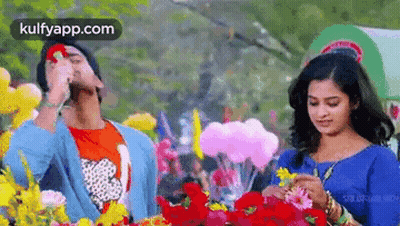 A Man And A Woman Are Standing Next To Each Other In A Field Of Flowers And Balloons . GIF