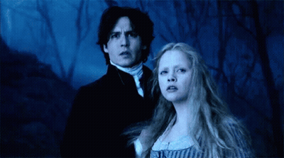 A Man And A Woman Are Standing Next To Each Other In A Forest . GIF