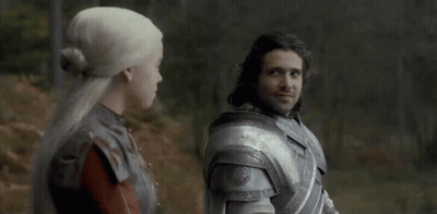 A Man And A Woman Are Standing Next To Each Other In A Forest . GIF