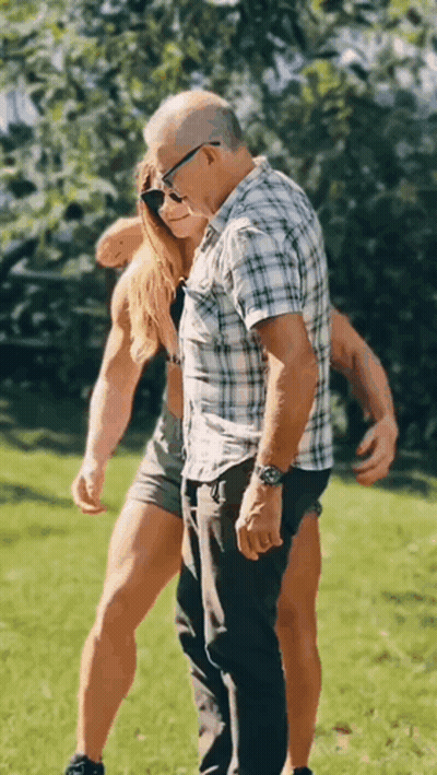 A Man And A Woman Are Standing Next To Each Other In A Grassy Field . GIF