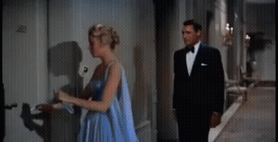 A Man And A Woman Are Standing Next To Each Other In A Hallway . The Woman Is Wearing A Blue Dress . GIF