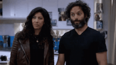 A Man And A Woman Are Standing Next To Each Other In A Kitchen . The Woman Is Wearing A Leather Jacket . GIF