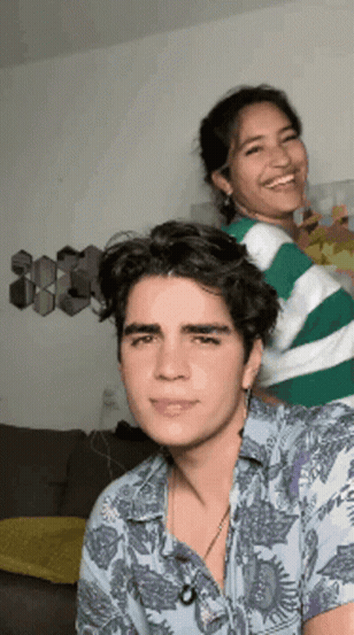 A Man And A Woman Are Standing Next To Each Other In A Living Room And Smiling . GIF