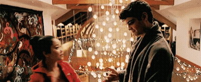 A Man And A Woman Are Standing Next To Each Other In A Living Room In Front Of A Christmas Tree . GIF