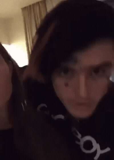 A Man And A Woman Are Standing Next To Each Other In A Room And Looking At The Camera . GIF