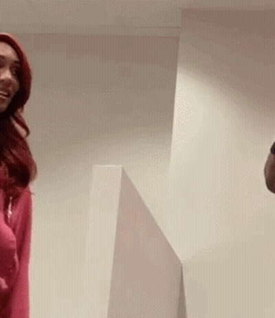 A Man And A Woman Are Standing Next To Each Other In A Room . The Woman Is Wearing A Pink Sweater . GIF