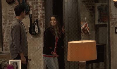 A Man And A Woman Are Standing Next To Each Other In A Room With Guitars On The Wall GIF