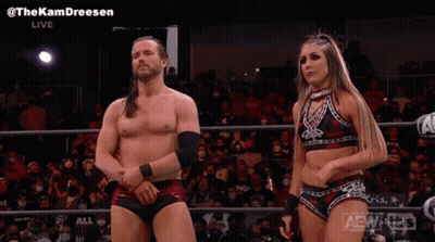 A Man And A Woman Are Standing Next To Each Other In A Wrestling Ring In Front Of A Crowd . GIF