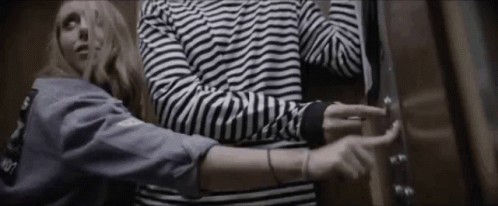 Man And Woman Standing In Elevator Woman In Striped Shirt GIF