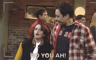 A Man And A Woman Are Standing Next To Each Other In Front Of A Brick Wall And A Camera . GIF